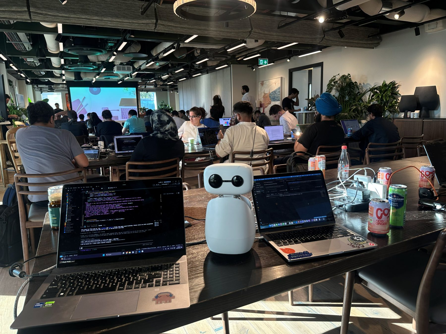 The Reachy Mini running OffBabel between our two laptops, with the hackathon in full swing behind it.